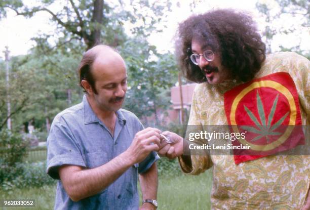 John Sinclair, political activist, wearing a large cannabis plant patch, smoking marijuana outdoors with John Rosevear in Ann Arbor, MI, in 1968.