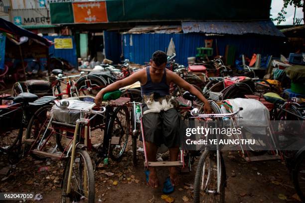 Myanmar trishaw driver sits with cat while waiting for customers in Yangon on May 24, 2018.