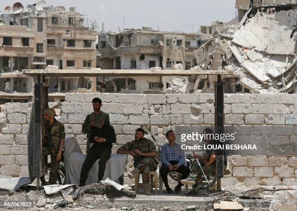 Syrian pro-government forces and civilians rest in the shade following a flag raising ceremony at the entrance of the Hajar al-Aswad neighbourhood on...