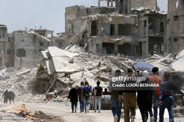 Syrian pro-government forces and civilians walk down a destroyed street following a flag raising ceremony at the entrance of the Hajar al-Aswad...