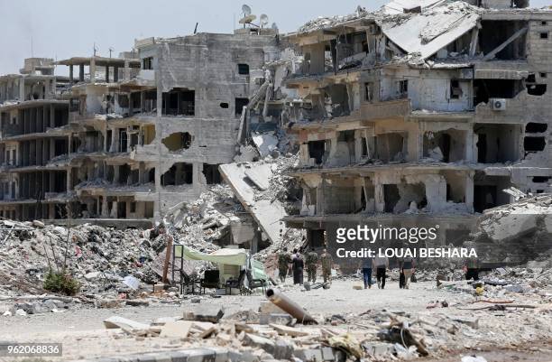 Syrian pro-government forces and civilians walk down a destroyed street following a flag raising ceremony at the entrance of the Hajar al-Aswad...