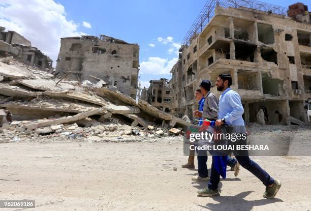 Pro-regime civilians walk down a destroyed following a flag raising ceremony at the entrance of the Hajar al-Aswad neighbourhood on the southern...