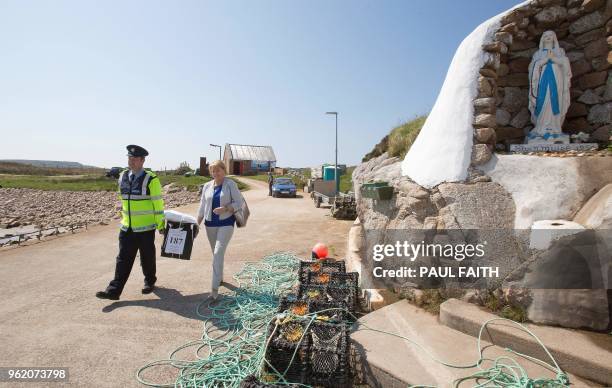 Garda officer Pat McElroy and Presiding officer Nancy Sharkey pass a shrine to the Virgin Mary as they carry a ballot box back to their transport...