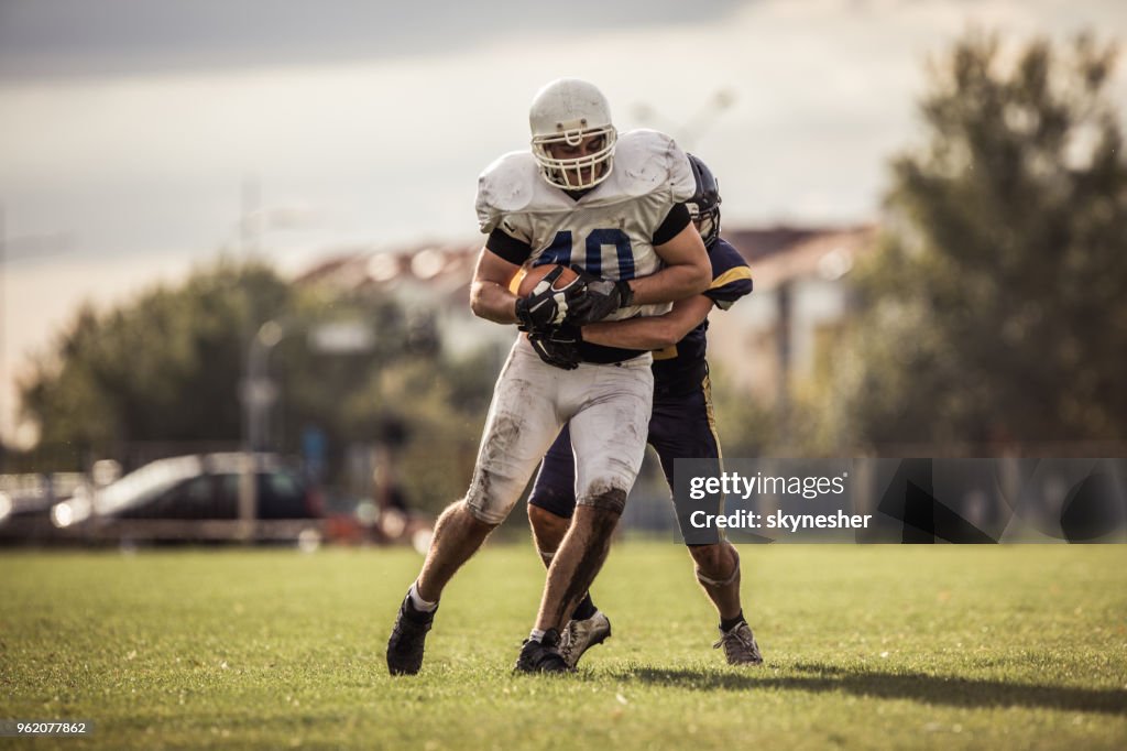 American football player caught by his opponent on playing field.