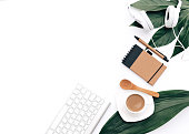 Creative flat lay background for blogger, keyboard, coffee cup and headphones with green leaves. Minimal workspace