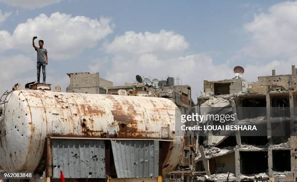 Syrian youth takes a photo on top of a bullet-riddled water container on the destroyed Thalateen Street in the Yarmuk Palestinian refugee camp on the...