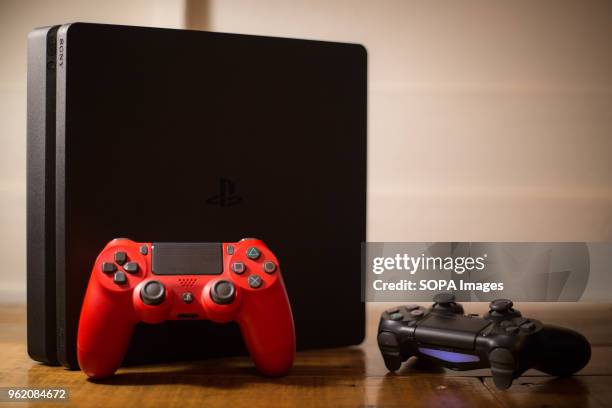 Sony PlayStation 4 video game console with a red and black wireless controllers next to it. The PlayStation 4 or PS4 is knows as the eighth...