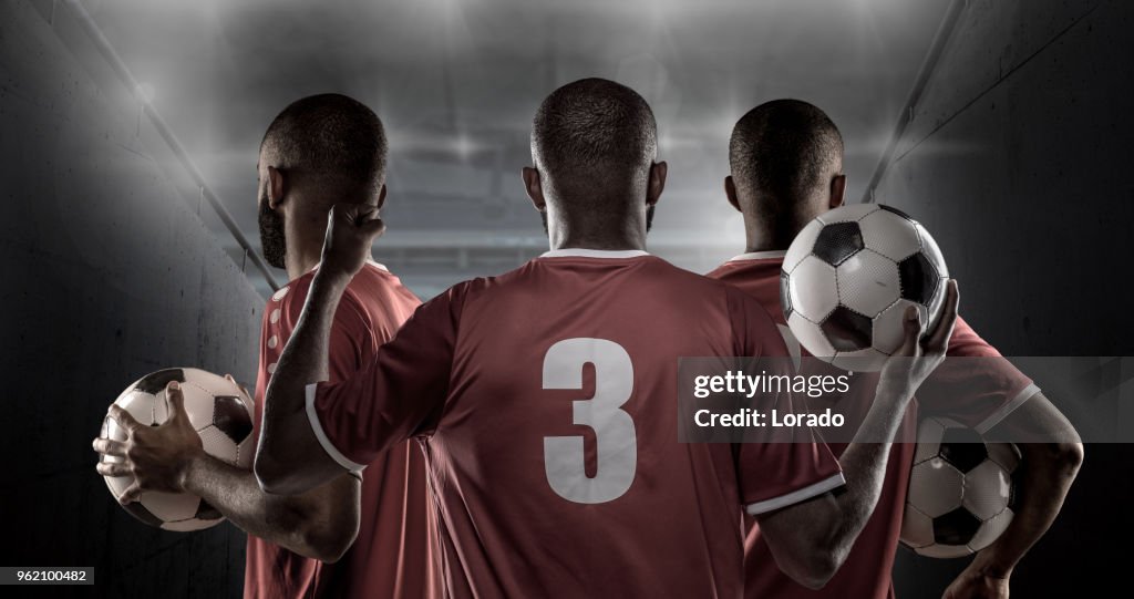 3 African Non-Caucasian Football Players Holding a Soccer Ball in front of Stadium Lights
