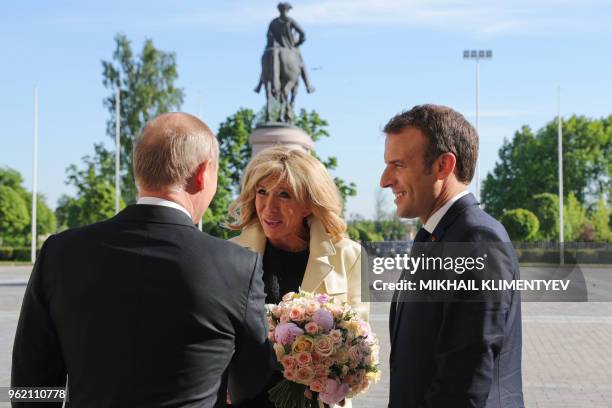 Russian President Vladimir Putin presents flowers to French First Lady Brigitte Macron as French President Emmanuel Macron stands nearby during a...