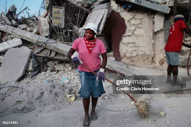 Woman working with an informal street sweeping crew cleans up a sidewalk in front of earthquake rubble January 27, 2010 in Port-au-Prince, Haiti....