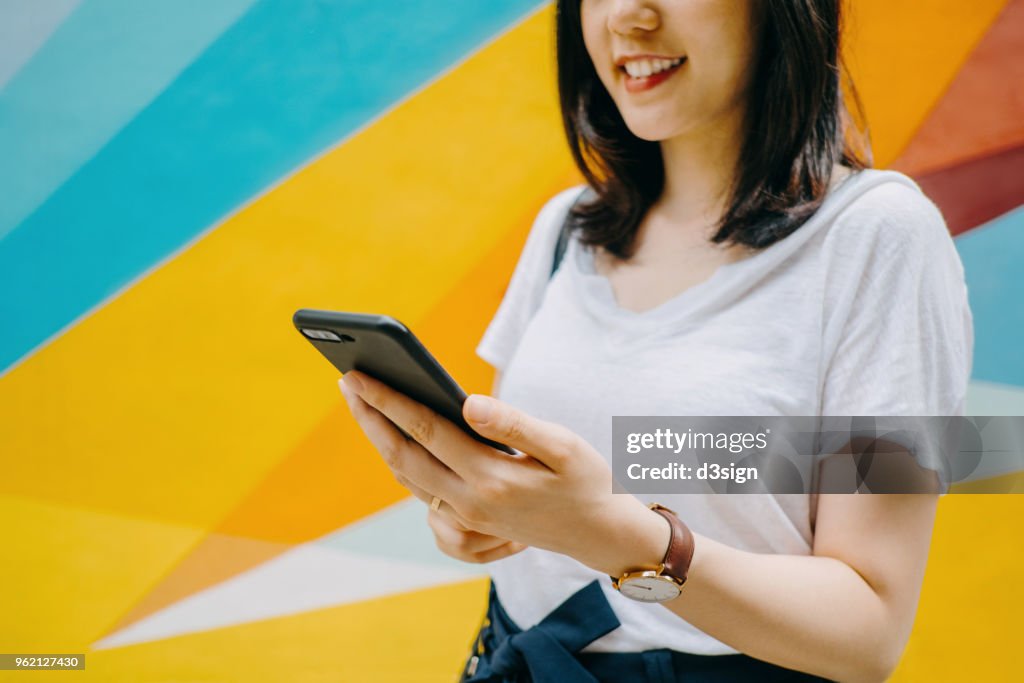 Portrait of smiling young woman using smartphone against colourful background in city