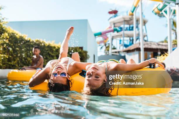 women looking at the camera on floaties in the swimming pool - water slide stock pictures, royalty-free photos & images