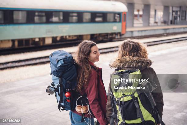 vrouwelijke paar, houdend handen en praten terwijl je op het perron van station - rugzaktoerist stockfoto's en -beelden
