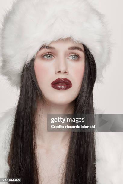 brunette woman with dark red lipstick blue eyes and white fur hat and - white lipstick stock-fotos und bilder