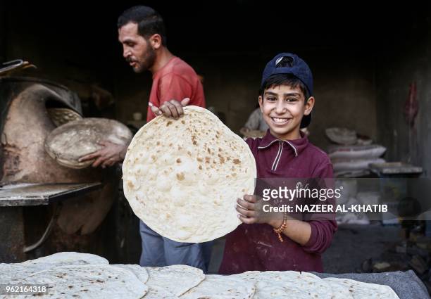 Syrian boy holds up freshly-baked traditional bread in a bakery in the northern town of al-Bab on May 24 to be consumed during the Iftar...