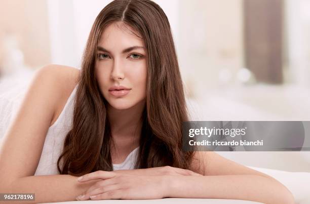 brunette woman with long hair laying on her bed - brunette woman bedroom stock-fotos und bilder