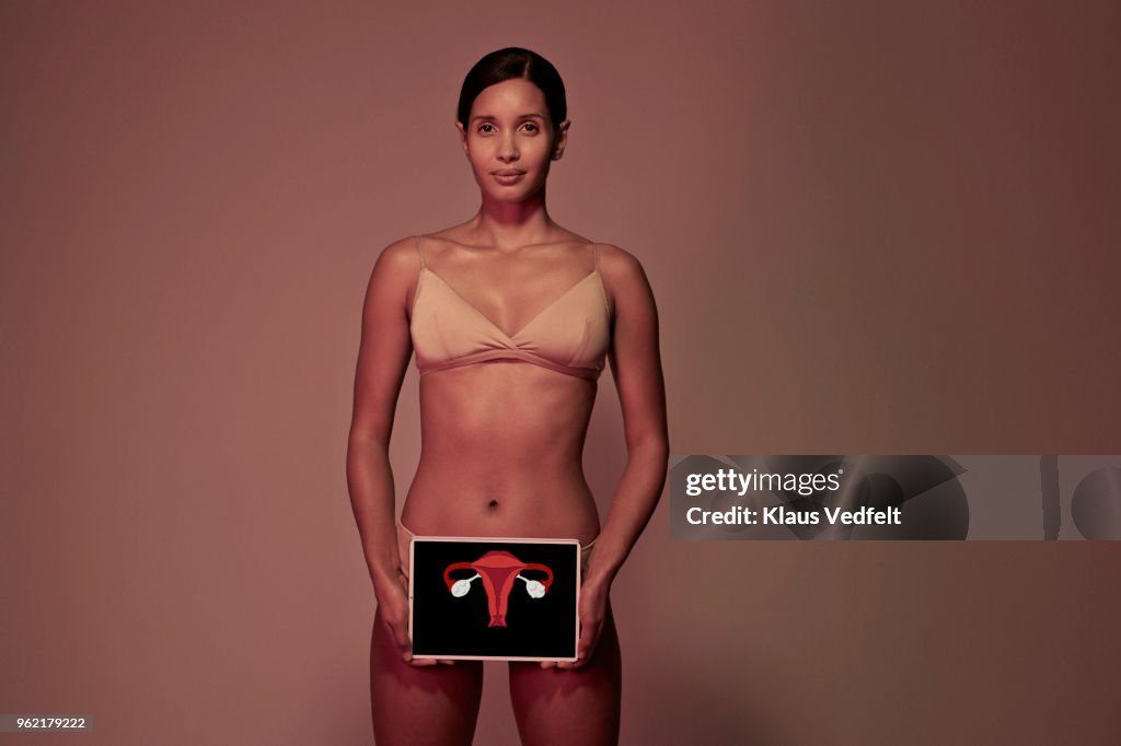 Young woman holding tablet in front of body to show womb & ovaries
