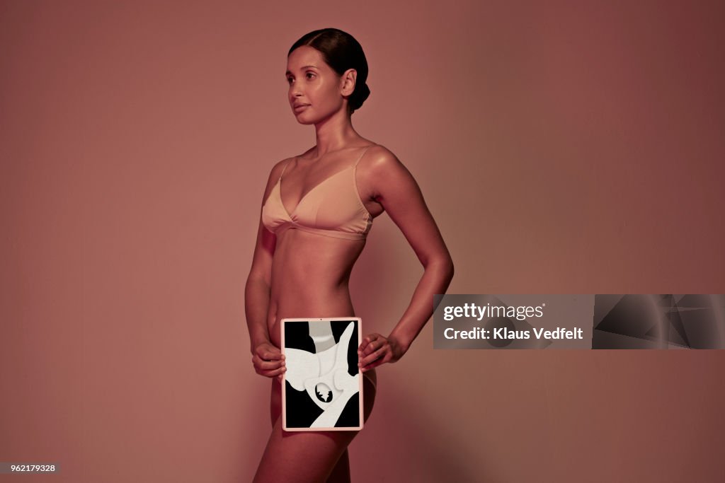 Young woman holding tablet in front of body to display hip bone