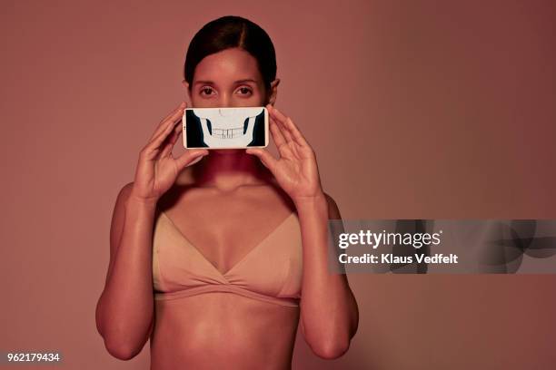young woman holding smartphone in front of mouth to show teeth & jaw bone - human jaw bone stockfoto's en -beelden