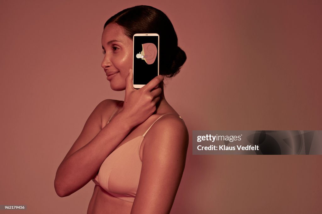Young woman holding smartphone on side of head to display inner ear