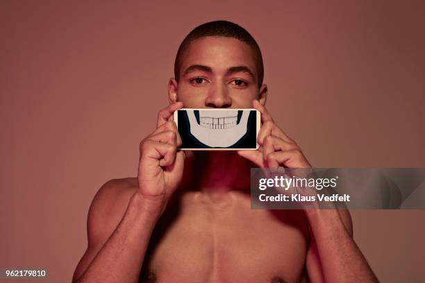 young man holding smartphone in front of mouth to show teeth & jaw bone - human jaw bone stock-fotos und bilder