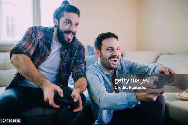 opgewonden vrienden spelen van videospellen - mannelijke vriendschap stockfoto's en -beelden