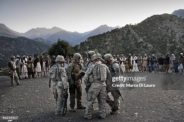 Afghan villagers stand in a line before the funeral of two children killed during an explosion as US Army soldiers of B Company, 2nd Battalion,12th...