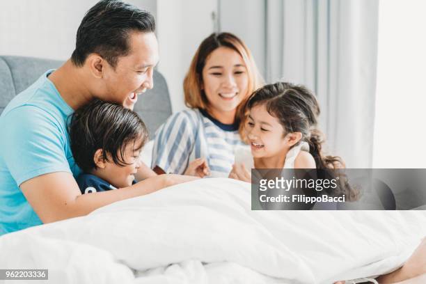gelukkige familie op het bed samen - asian young family stockfoto's en -beelden