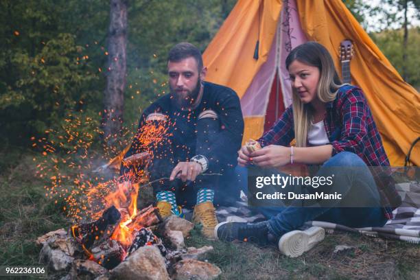 happy couple fried sausages on bonfire in the forest - couple grilling stock pictures, royalty-free photos & images