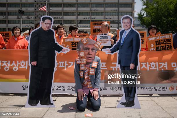 An anti-US protester wearing a face-mask depicting US president Donald Trump kneels between cardboard cutouts of North Korean leader Kim Jong Un and...