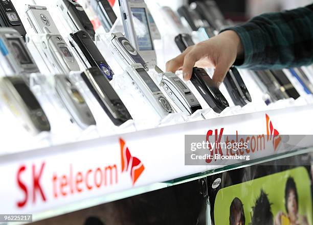 Mobile phones are displayed for sale on a shelf with an SK Telecom advertising board at an electronics shop in Seoul, South Korea, on Thursday, Jan....