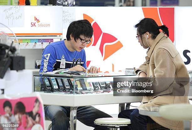 Sales clerk helps a customer at an electronics shop where an SK Telecom Co. Advertising board is displayed, in Seoul, South Korea, on Thursday, Jan....