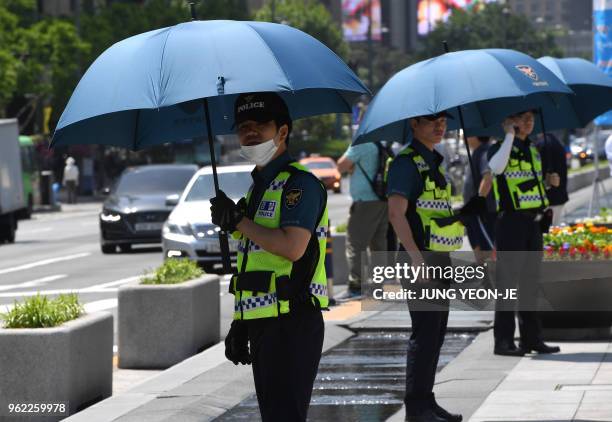 Police officers carry umbrellas during a rally by anti-Trump protesters near the US embassy in Seoul on May 25, 2018. - South Korea's Unification...