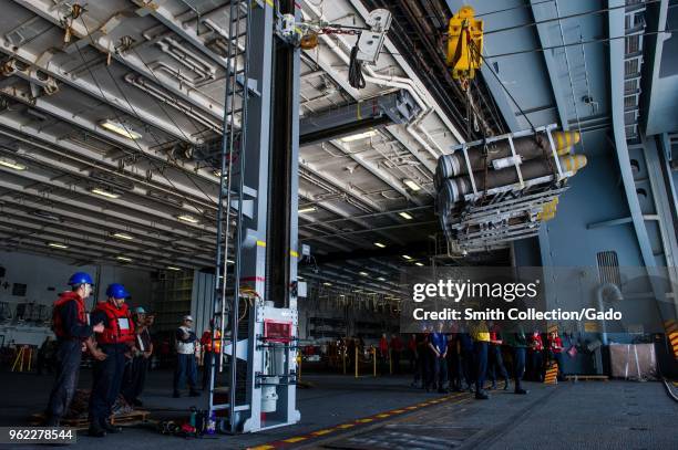 Photograph of navy soldiers receiving bombs in the hangar bay aboard the aircraft carrier USS Ronald Reagan during a replenishment-at-sea, May 15,...