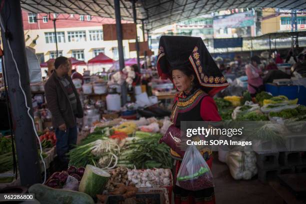 Woman wearing traditional clothes seen buying vegetable at a local market near the Tiger Leaping Gorge.