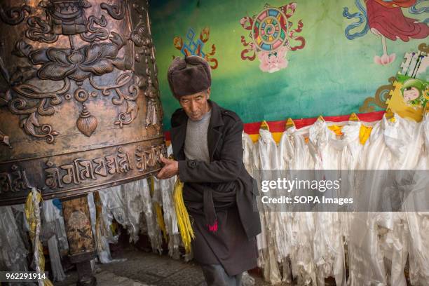 An old man seen turning a large prayer wheel at the Tibetan Buddhist Ganden Sumtseling Monastery in Shangri-La.