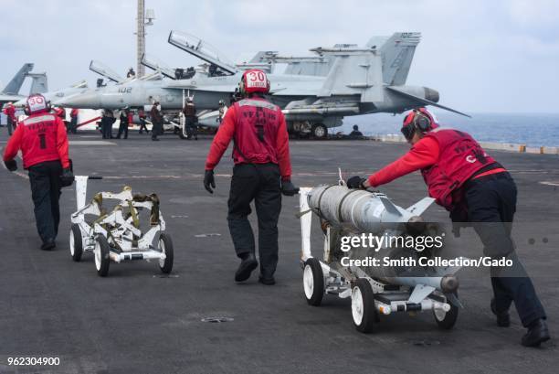 Photograph of navy sailors transporting bombs on the flight deck of the Nimitz-class aircraft carrier USS Harry S Truman, fighter jets visible in the...