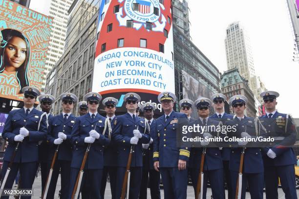 Photograph of Rear Admiral Steven Poulin with members of the Coast Guard Drill Team standing beneath the Nasdaq Marquee as it displays a message of...