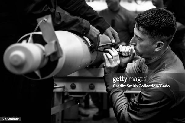 Photograph of Aviation Ordnanceman 1st Class John Baird working on a simulated bomb build aboard the aircraft carrier USS George HW Bush as part of a...