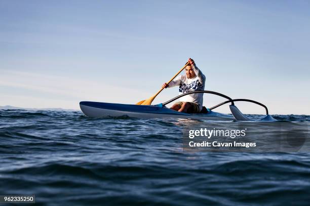 mature man rowing outrigger on sea against clear sky during sunny day - outrigger stock pictures, royalty-free photos & images