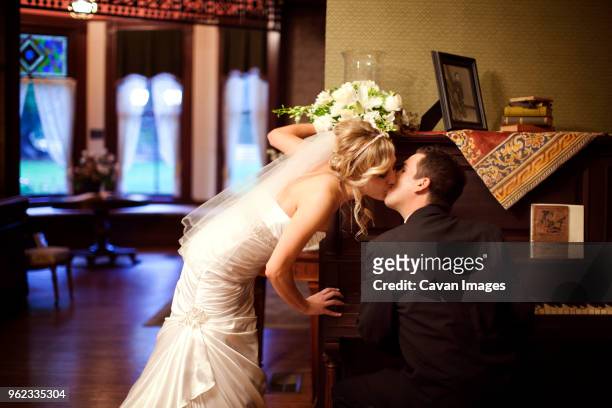 bride and groom kissing while sitting at piano during wedding day - piano rose stock pictures, royalty-free photos & images