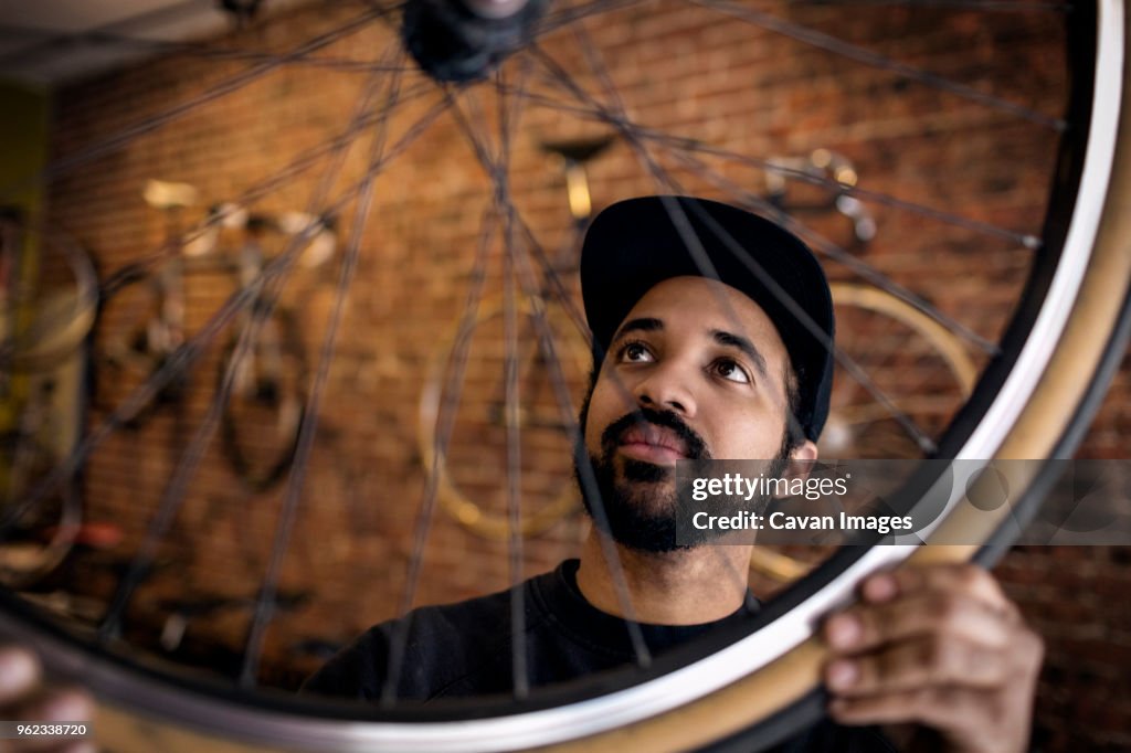 Man examining bicycle wheel while standing in workshop
