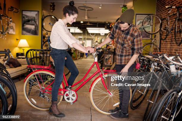 man looking at customer sitting on bicycle in workshop - bike shop stock pictures, royalty-free photos & images