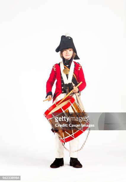 portrait of boy playing drum while standing against white background - revolutionary war uniform stock pictures, royalty-free photos & images