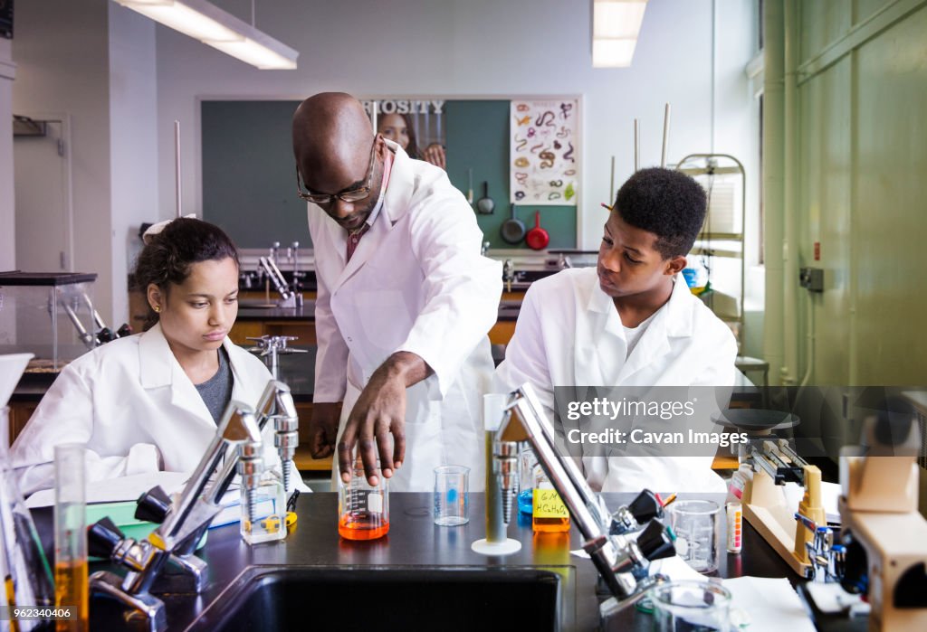 Teacher teaching scientific experiment to students in high school laboratory