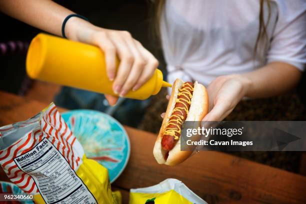 cropped image of woman pouring mustard sauce on hot dog at garden party - pouring sauce stock pictures, royalty-free photos & images