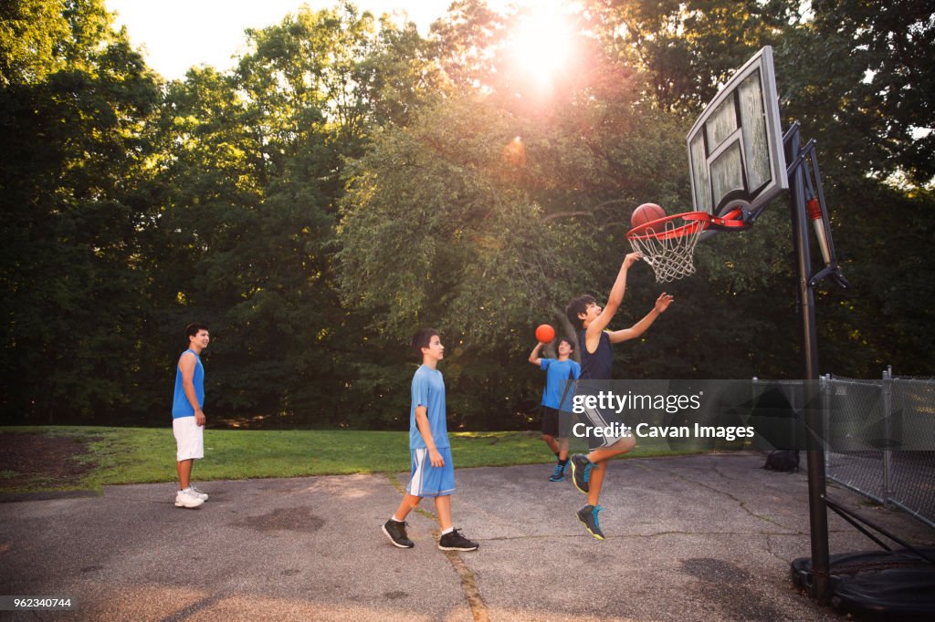 Players playing basketball at court against trees on sunny day
