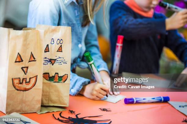 smiley faces on paper bags by siblings making art at table during halloween party - halloween craft stock pictures, royalty-free photos & images