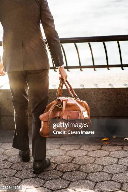 low section of businessman carrying bag while standing at railing against sky - spallina foto e immagini stock