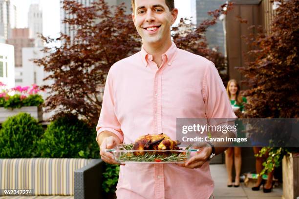 midsection of smiling man carrying roasted chicken in tray while standing against plants - man tray food holding stockfoto's en -beelden